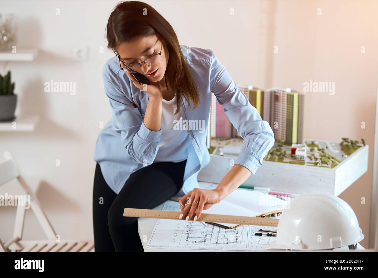 Successful attractive engineer drawing house draft and making a phone ...