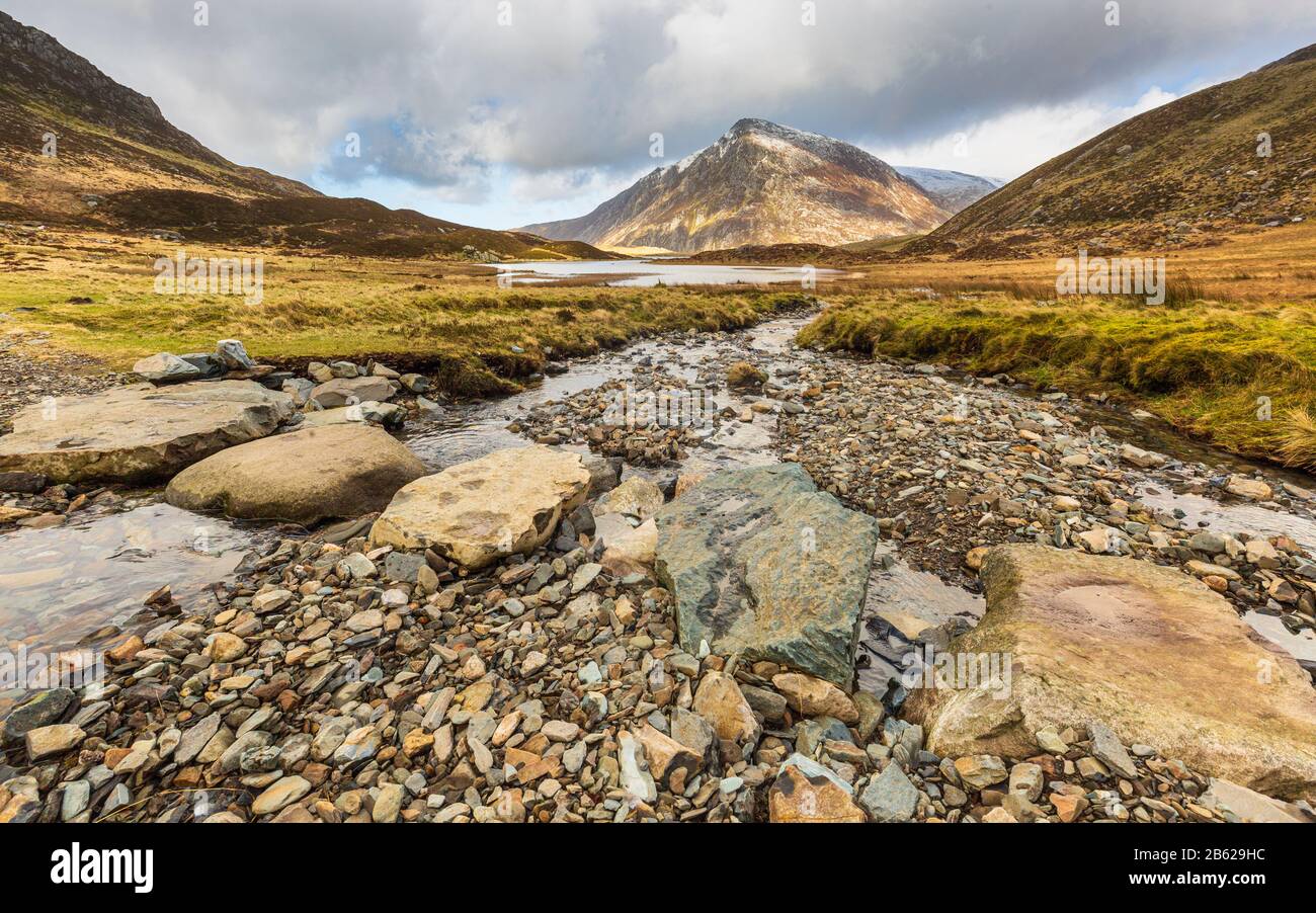 Stepping stones across melt water from snow covered Glyder Fawr leading to Llyn Idwal with Pen yr Ole Wen in the background,Snowdonia, North Wales Stock Photo