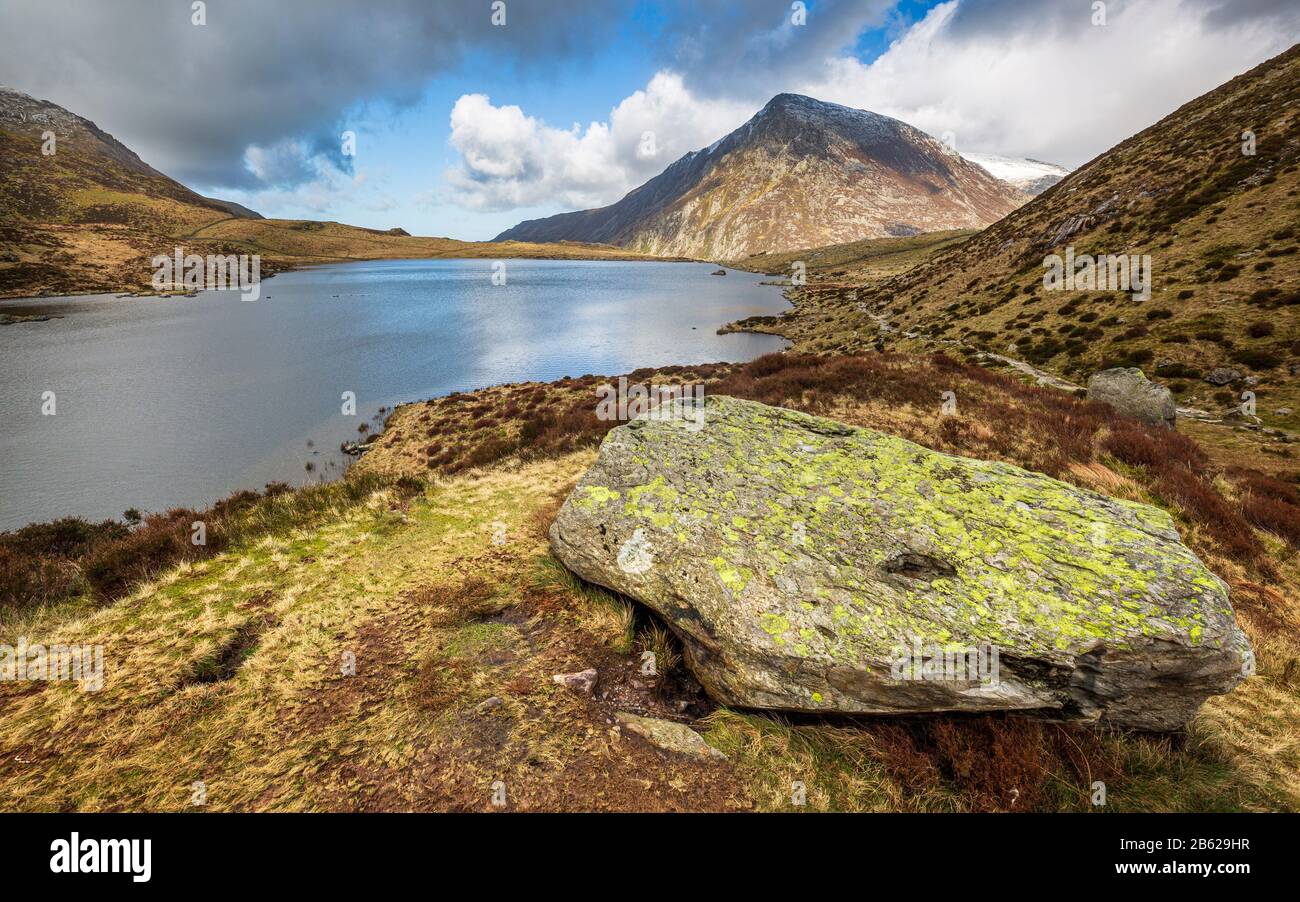 A large boulder on the shore of Llyn Idwal with Pen yr Ole Wen mountain in the background, Snowdonia National Park, North Wales Stock Photo