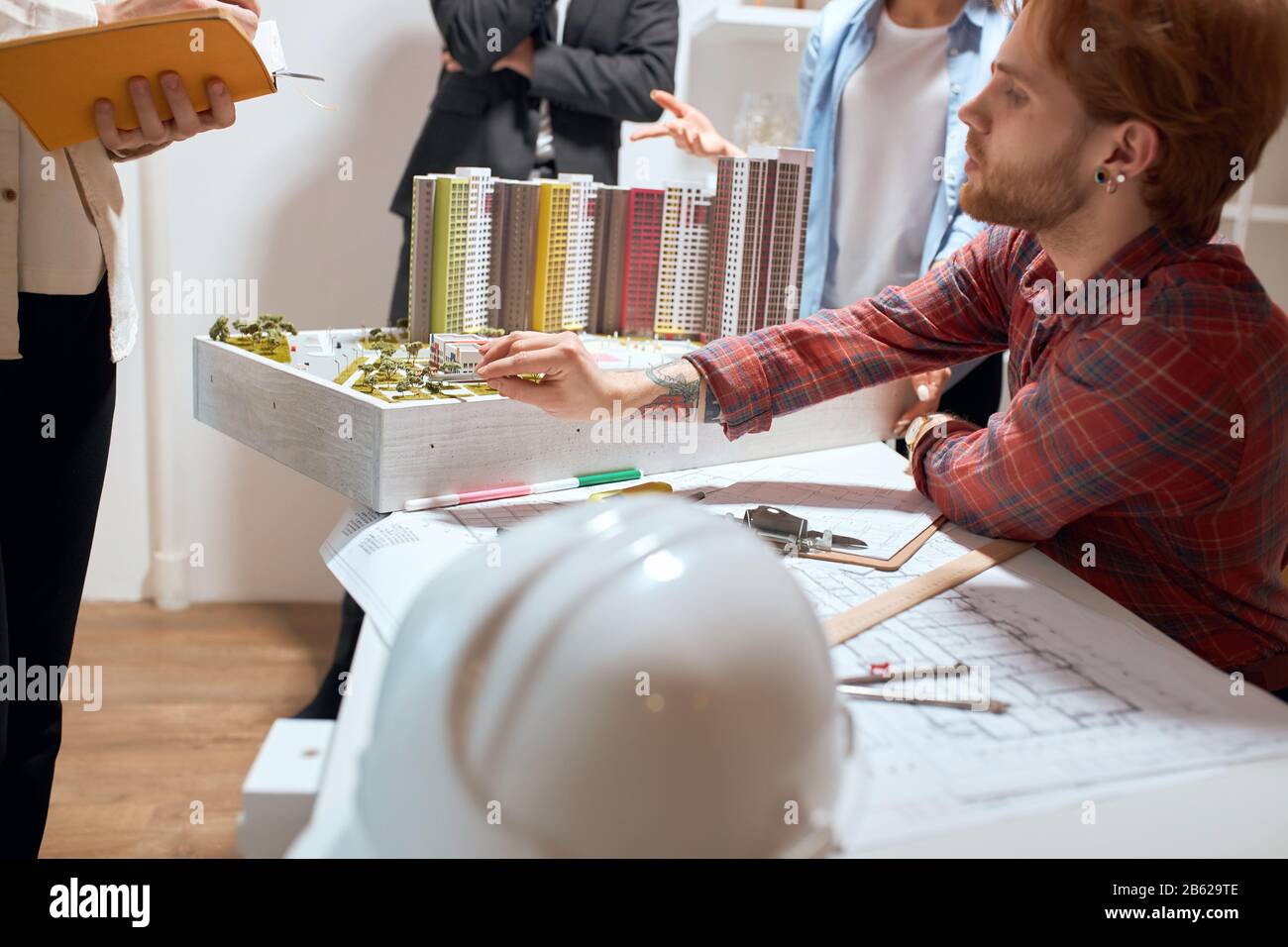 young ginger handsome man in stylish red shirt pointing to the model with a pen, talking about features of project to his colleagues during the meetin Stock Photo