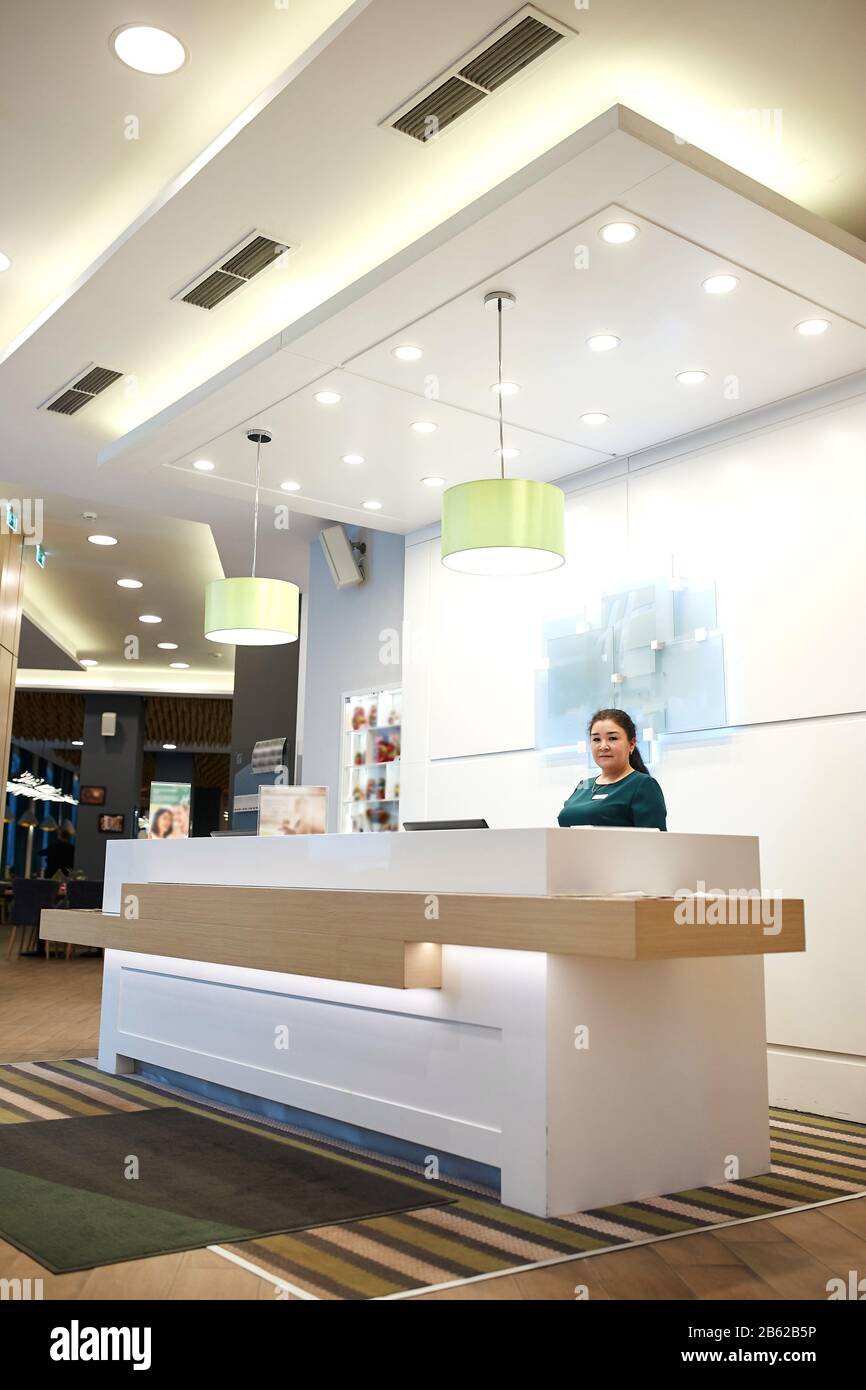 friendly female receptionist worker standing at luxury hotel counter, waiting for guests. close up side view photo, job, profession, occupation Stock Photo