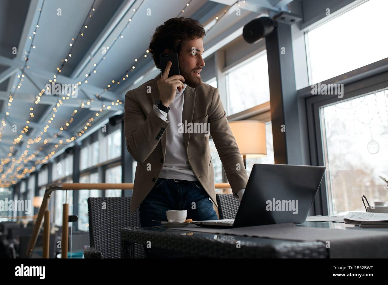 pleasant smart manager talking with colleagues, partners with smart phone, looking aside, at the window. Stock Photo
