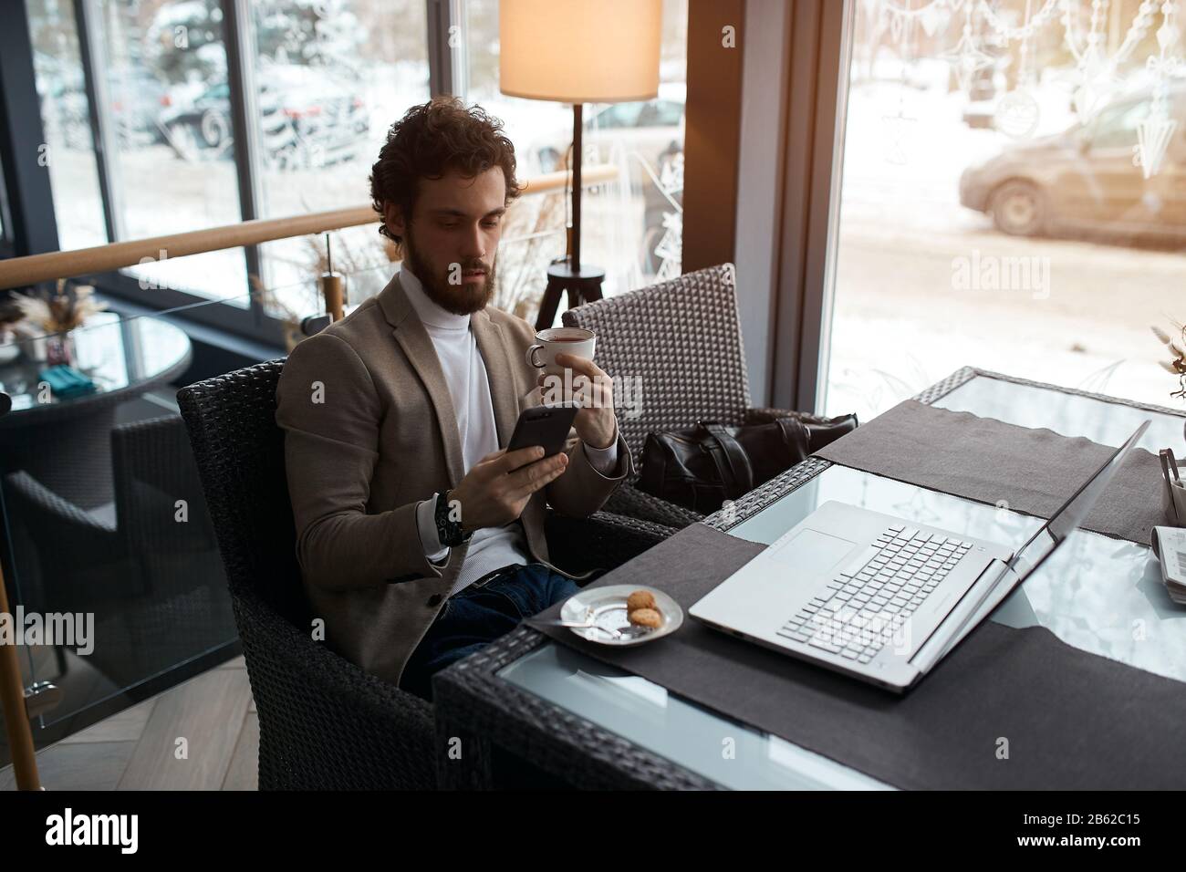 bearded pleasant man is concentrated on texting sms, best friend, man holding a cup and using smart phone . close up photo Stock Photo