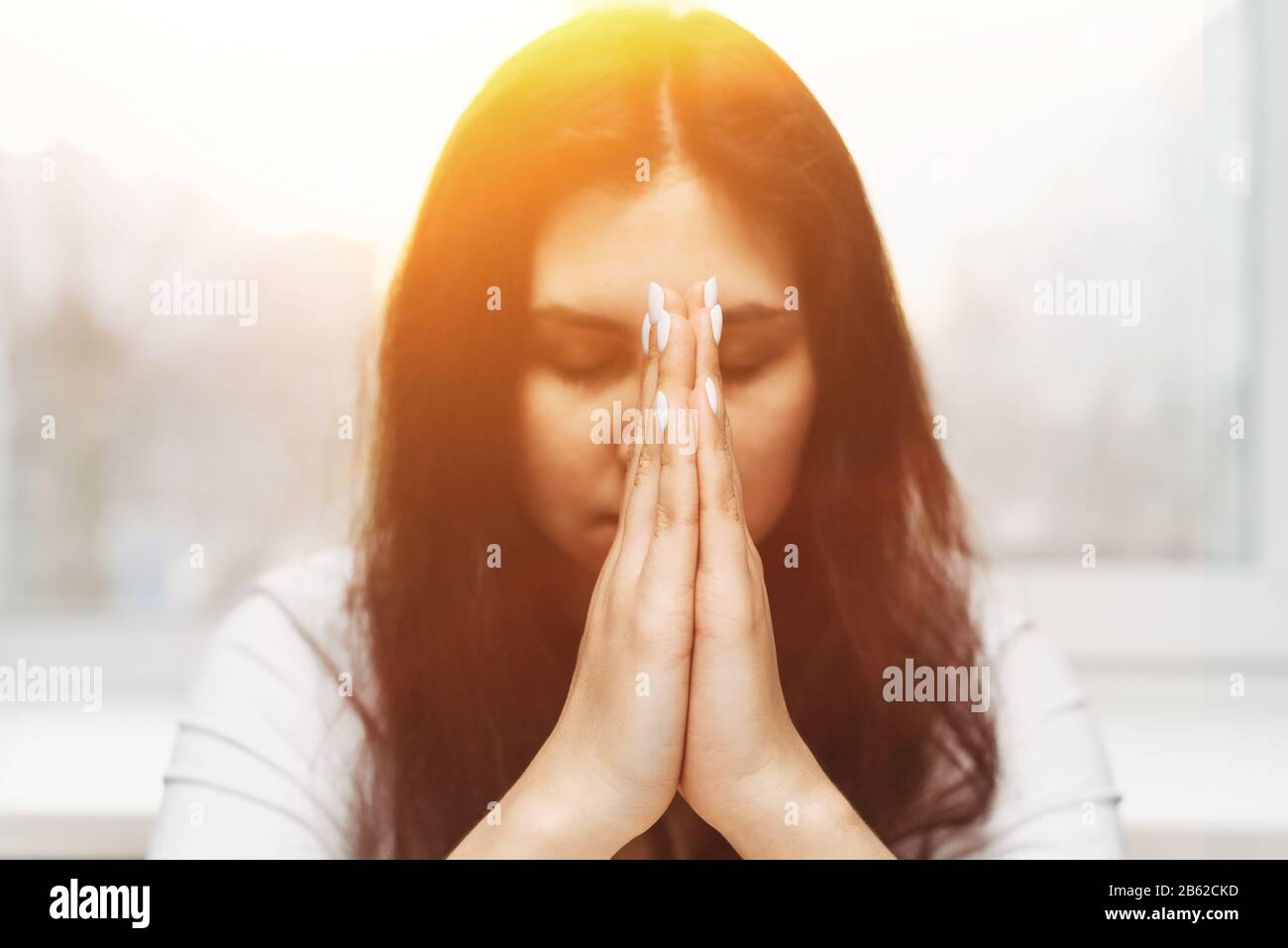 Cute beautiful girl folded her hands in prayer. A woman asks God for help. Stock Photo