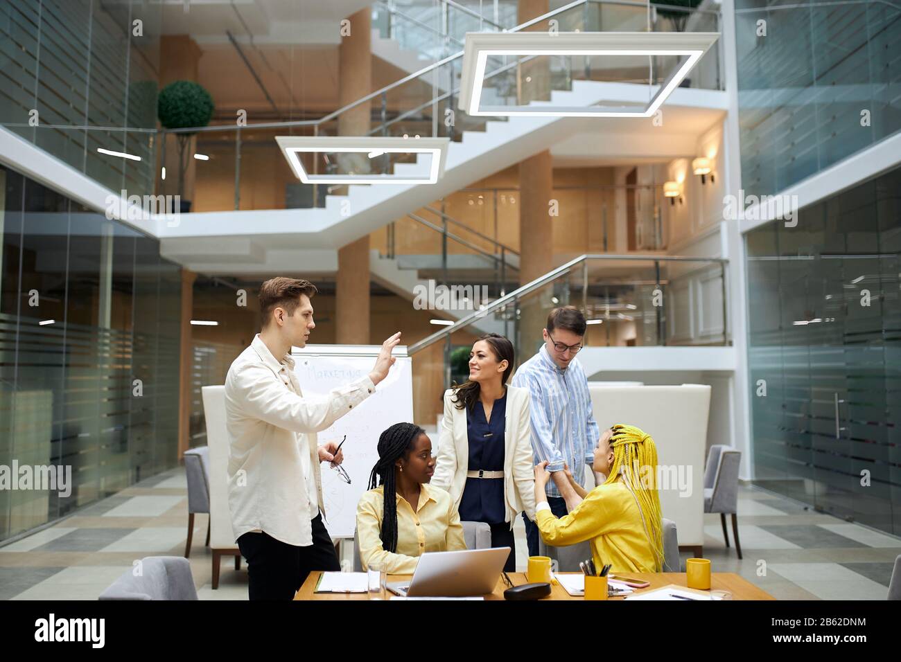 young diverse people having a rest after meeting, conversation. women and men taking part in the experiment, guy in glasses and white shirt running a Stock Photo