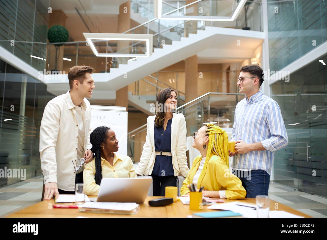cheerful young people in stylish casual clothes looking at each other in the office, business people having fun, trying to find out who is ling. Stock Photo