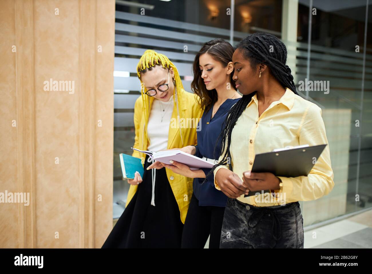 brunette woman holding a book, notebook, showing her plans, presenting her project while walking with colleagues in the office building. close up side Stock Photo