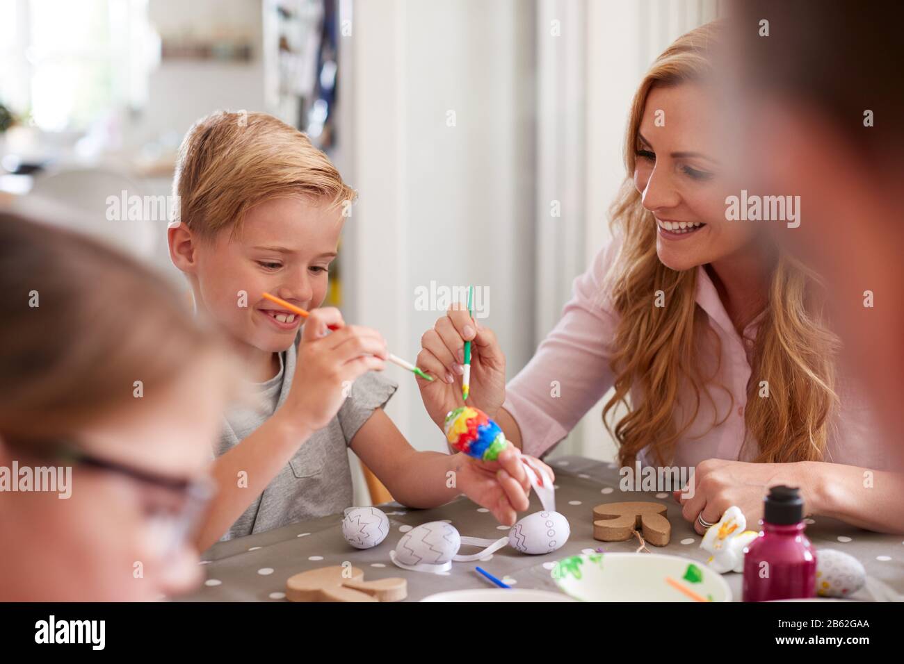 Parents With Children Sitting At Table Decorating Eggs For Easter At Home Stock Photo