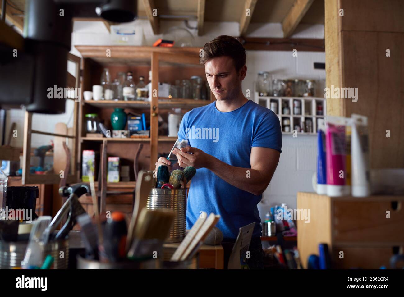 Man In Workshop Choosing Paintbrush For Upcycling And  Craft Projects Stock Photo