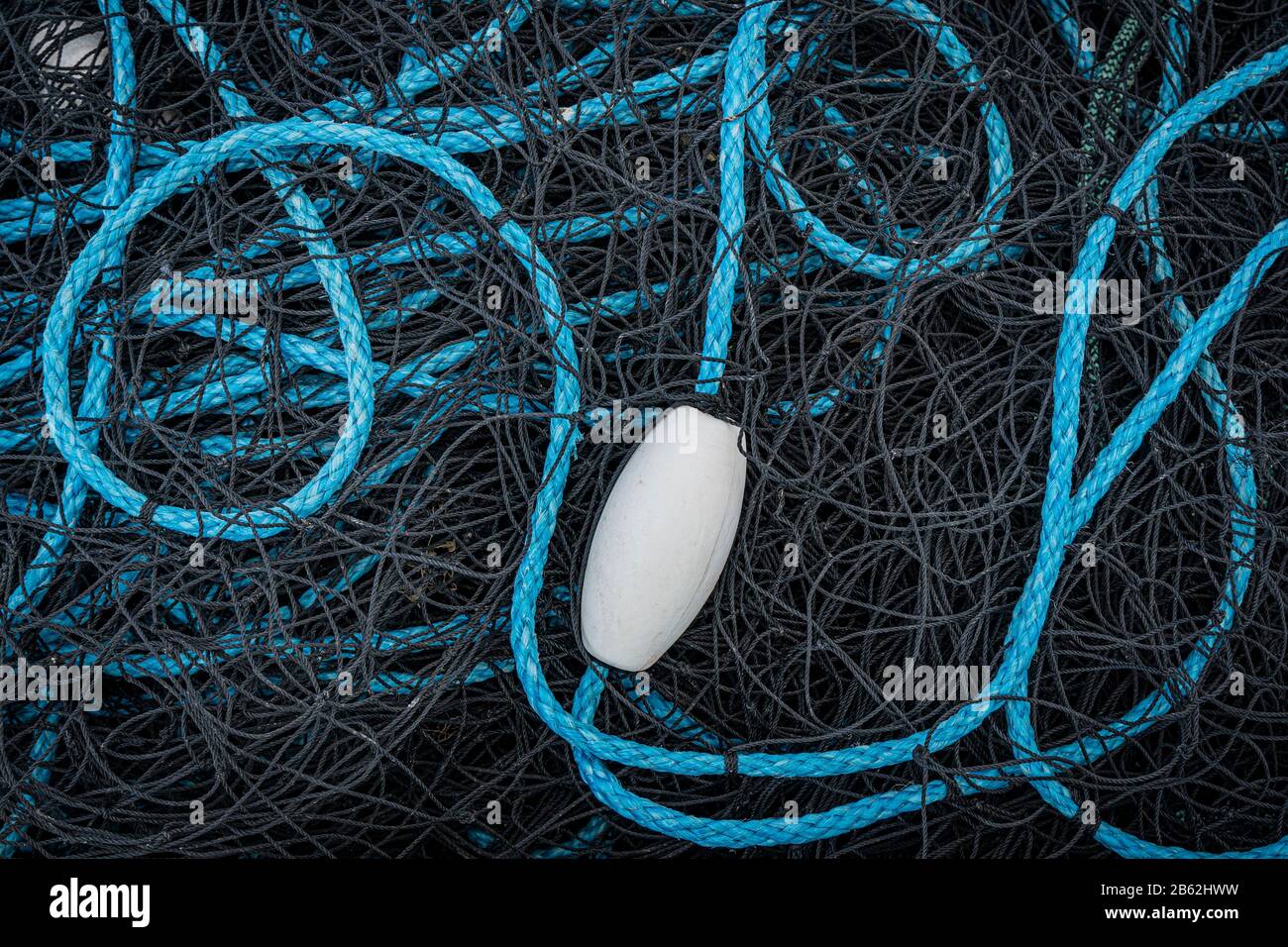 A jumble of black fishing nets with a tangled blue rope and a white float Stock Photo