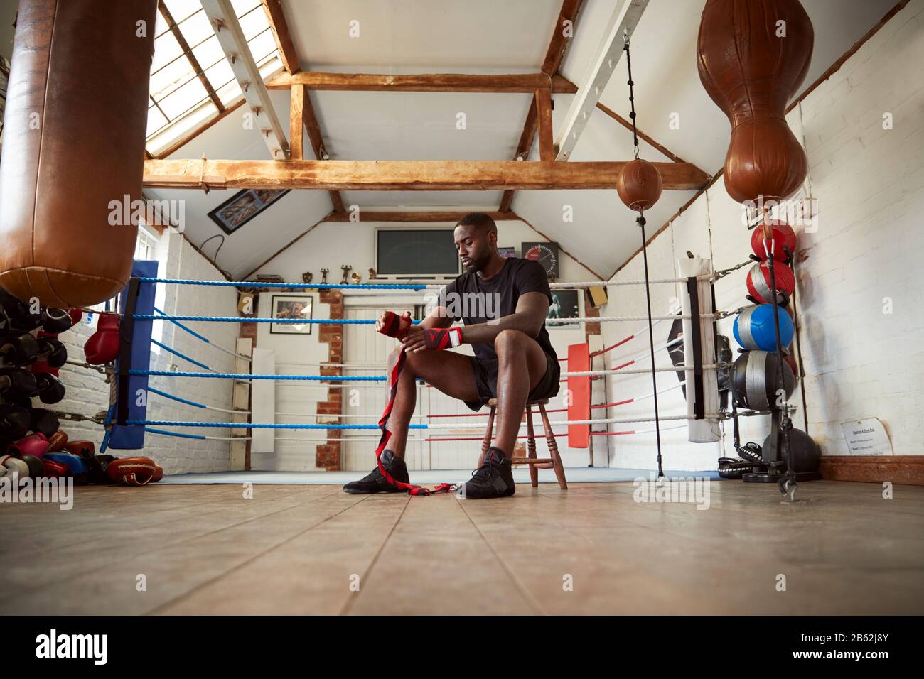 Male Boxer Training In Gym Sitting Next To Boxing Ring Putting Wraps On