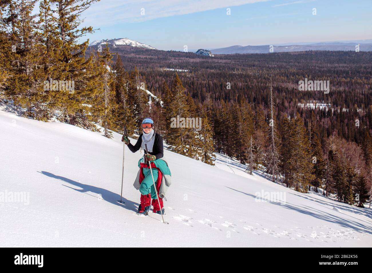 A female climber , dressed in red, climbs up a snowy slope of mountain. Winter clear sky day. In background Ural mountains, russia Stock Photo