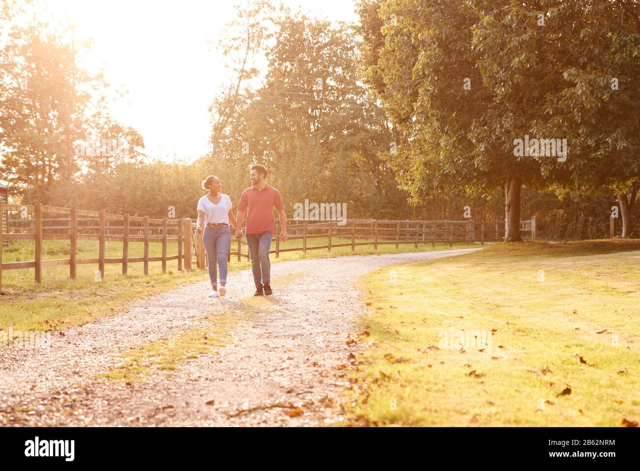 Romantic Couple Walking Hand In Hand Along Country Lane At Sunset Stock ...