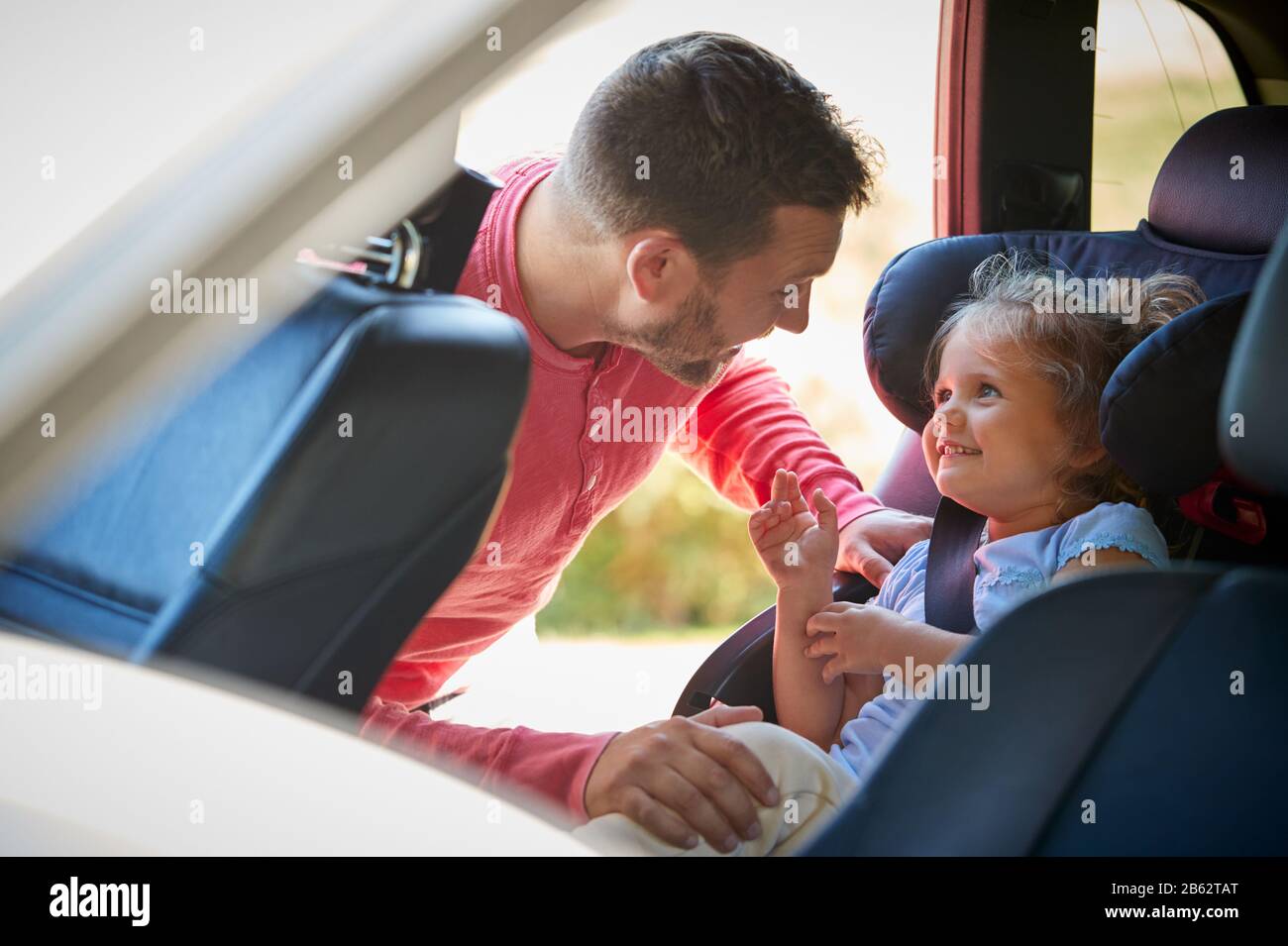 Father Securing Daughter Into Rear Child Seat Before Car Journey Stock Photo