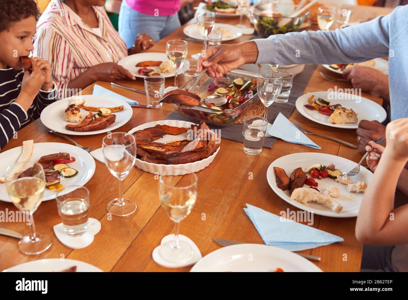 Close Up Of Multi-Generation Family Sitting Around Table Enjoying Meal At Home Together Stock Photo