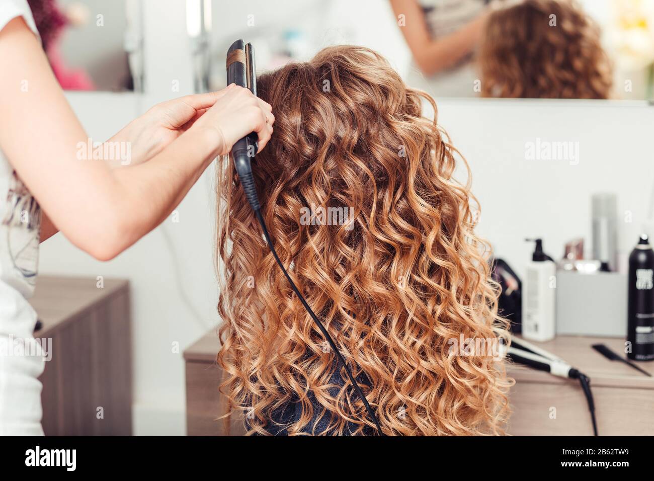 Hairdresser curling woman hair with electric iron curler tong. Hairstylist  making girl hairstyle Stock Photo - Alamy