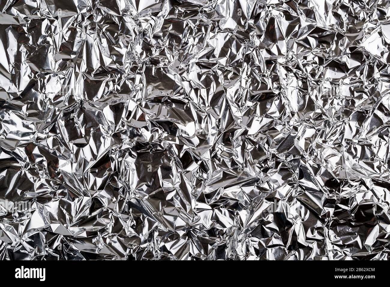 Crumpled aluminum foil texture. Sheet of creased silver foil with shiny folds for background. Metal wrinkled surface as graphic resource. Top view. Stock Photo