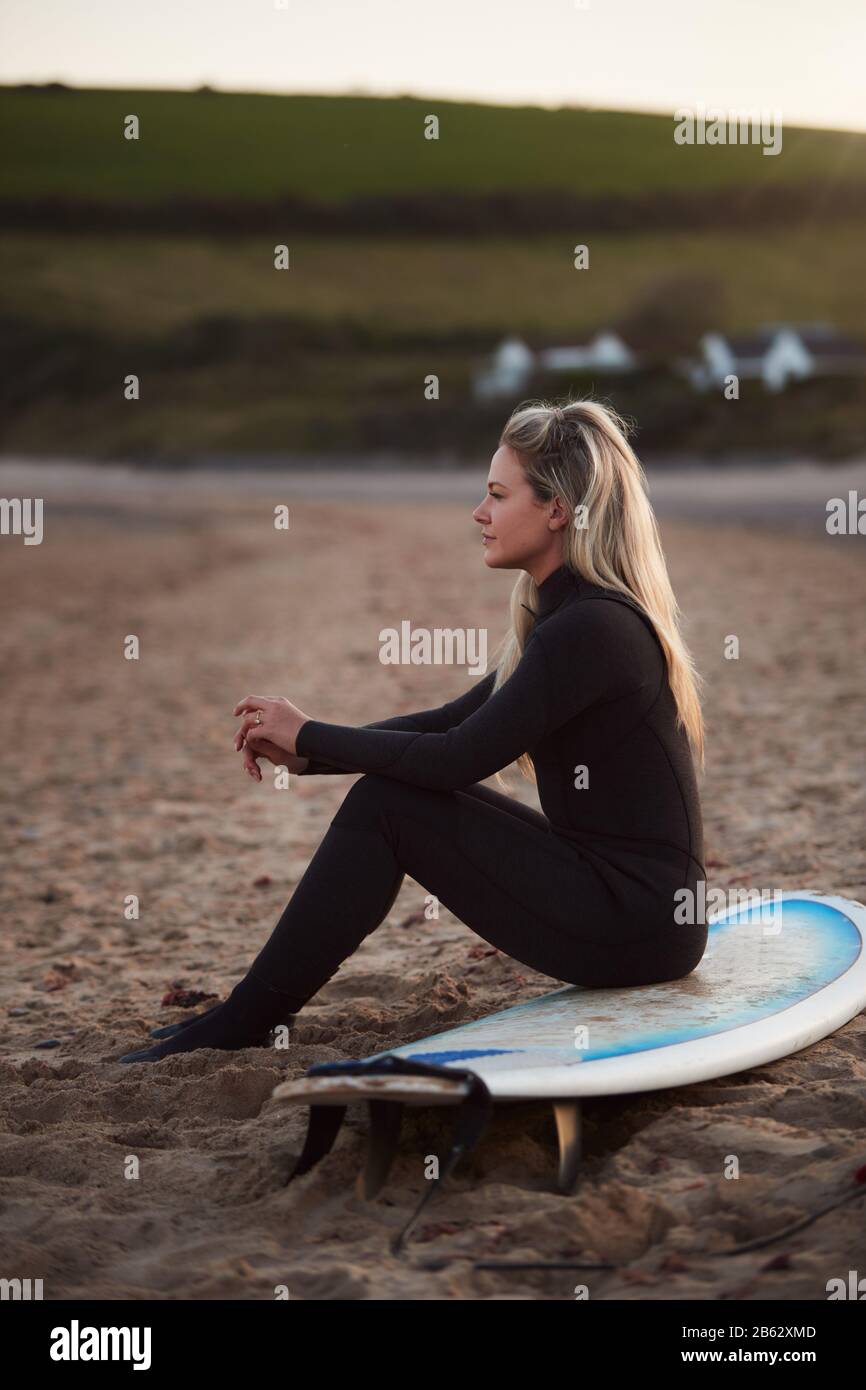 Side View Of Thoughtful Woman Wearing Wetsuit On Surfing Staycation Looking Out To  Sea At Waves Stock Photo