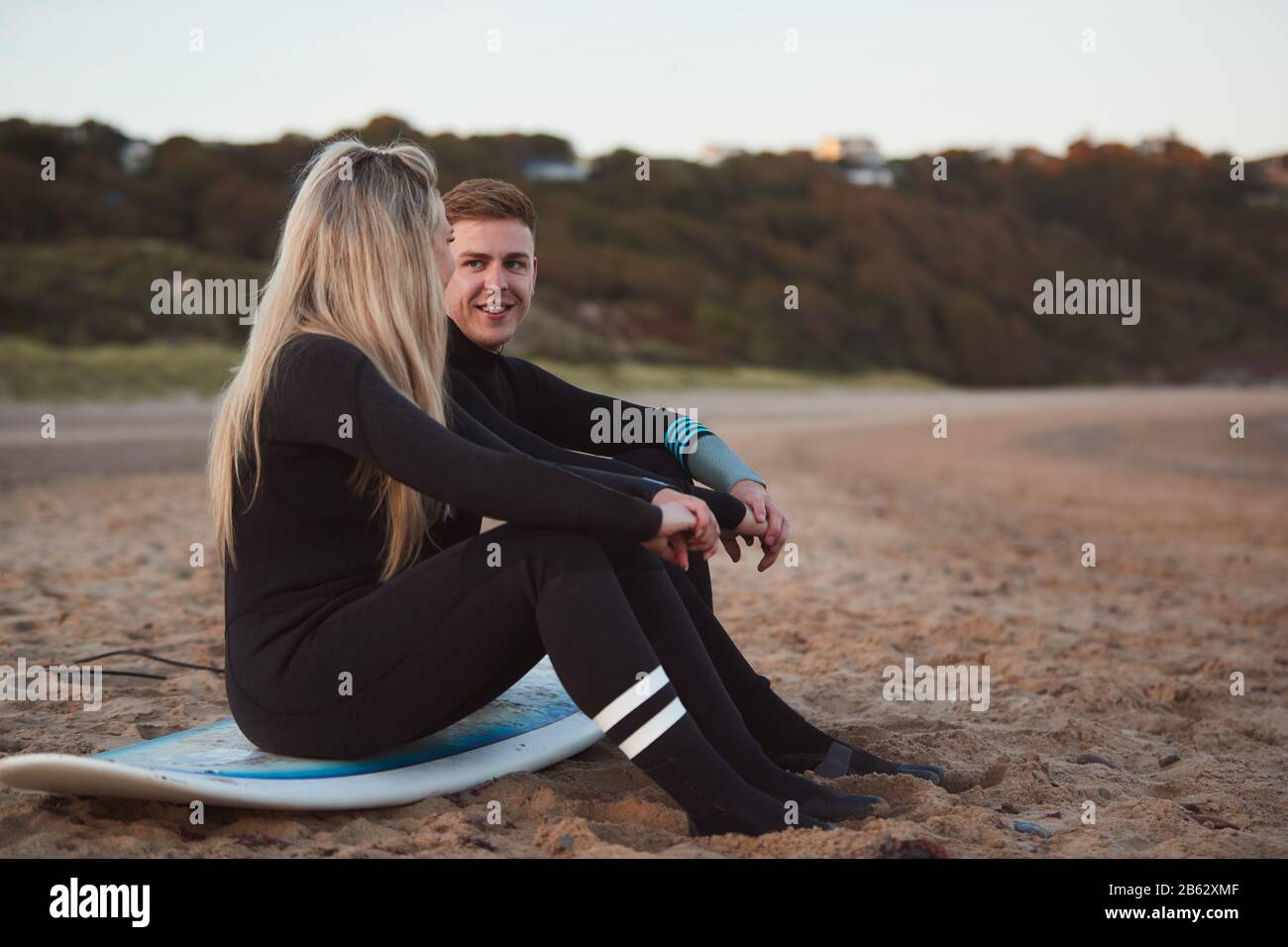 Couple Wearing Wetsuits On Surfing Staycation Sitting On Surfboard