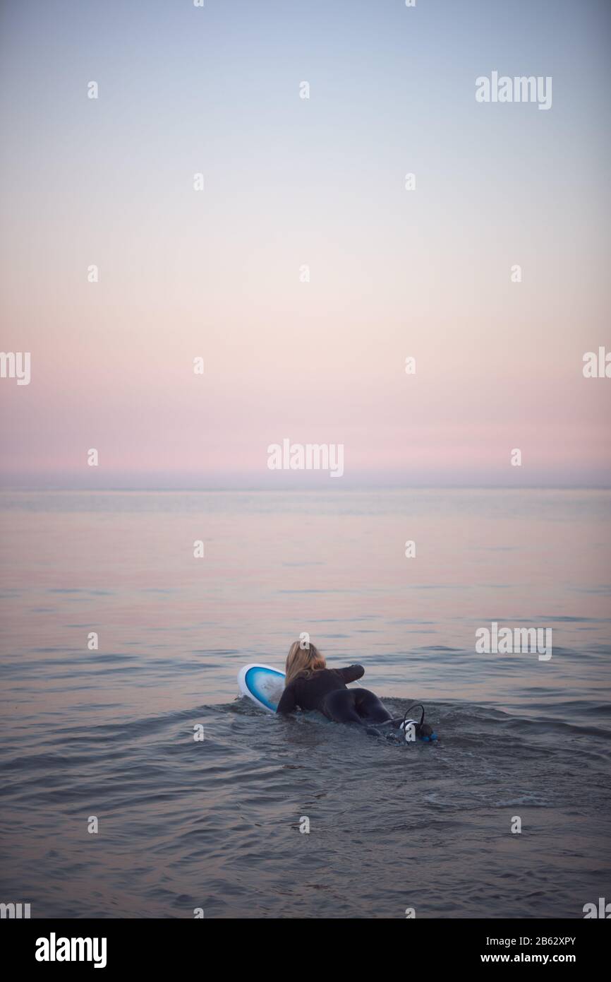 Woman Wearing Wetsuit Paddling Floating Surfboard Out Onto Calm  Sea Stock Photo