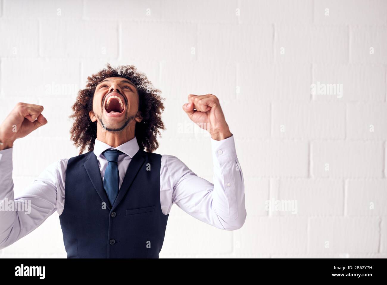 Happy Young Businessman Wearing Suit Celebrating Standing Against White Studio Wall Stock Photo