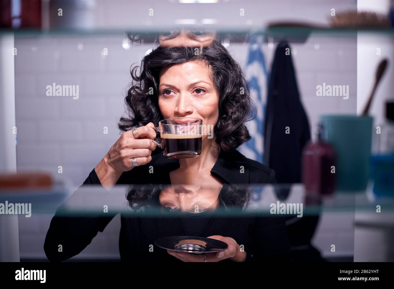 View Through Bathroom Cabinet Of Mature Businesswoman Drinking Coffee Stock Photo
