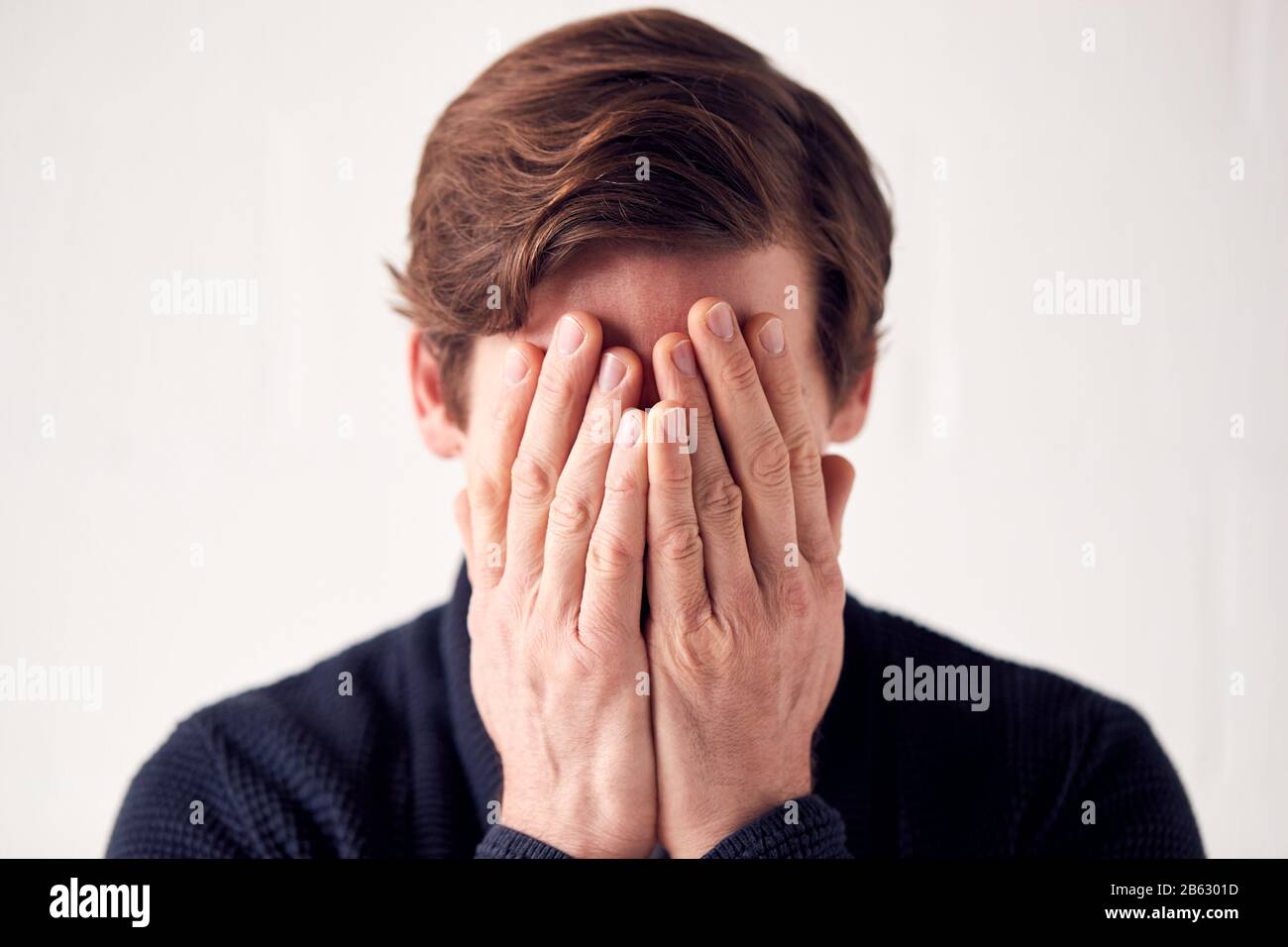 Studio Shot Of Unhappy Man Covering Face With Hands Stock Photo