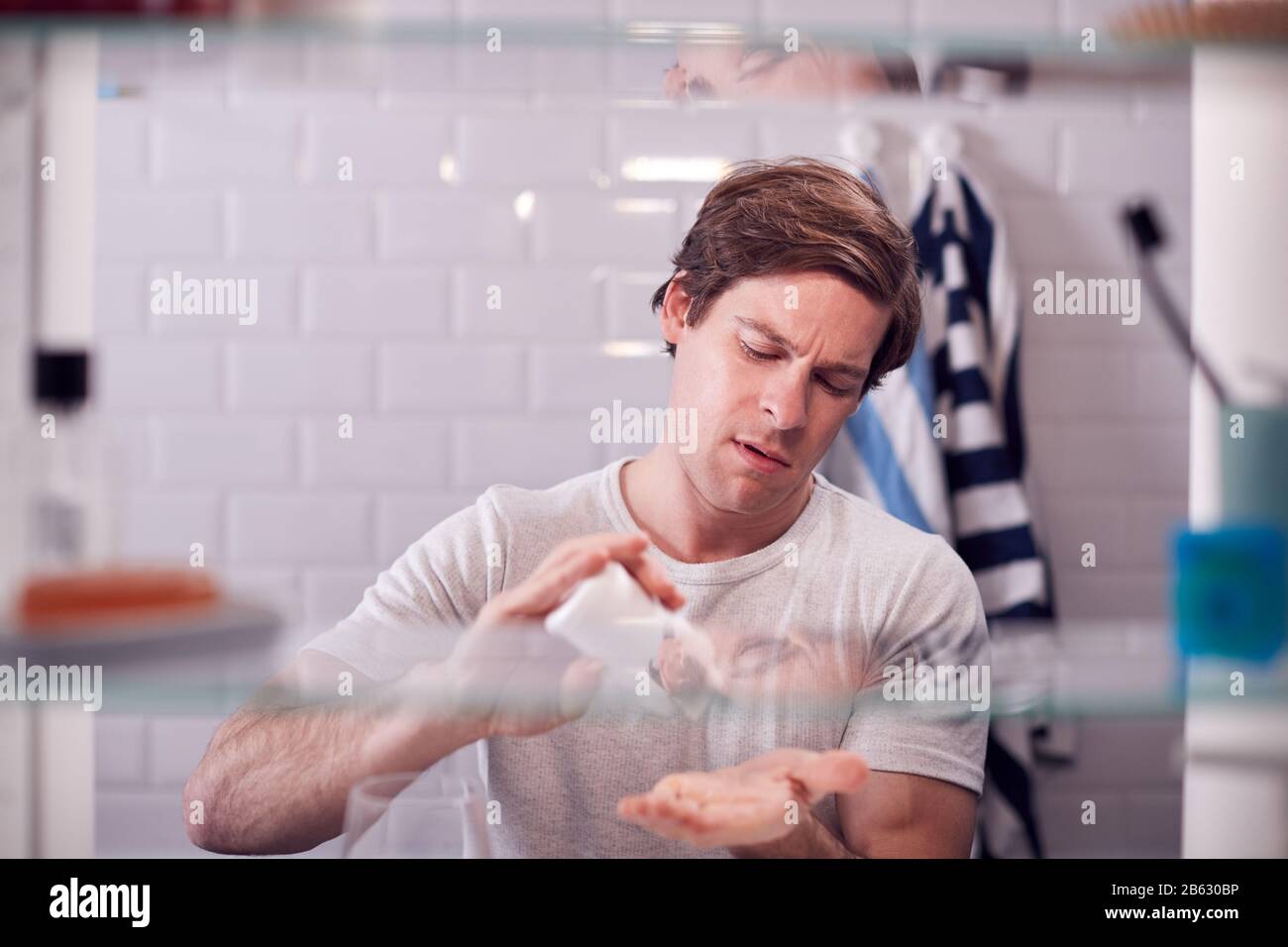 View Through Bathroom Cabinet Of Man Taking Medication From Container Stock Photo