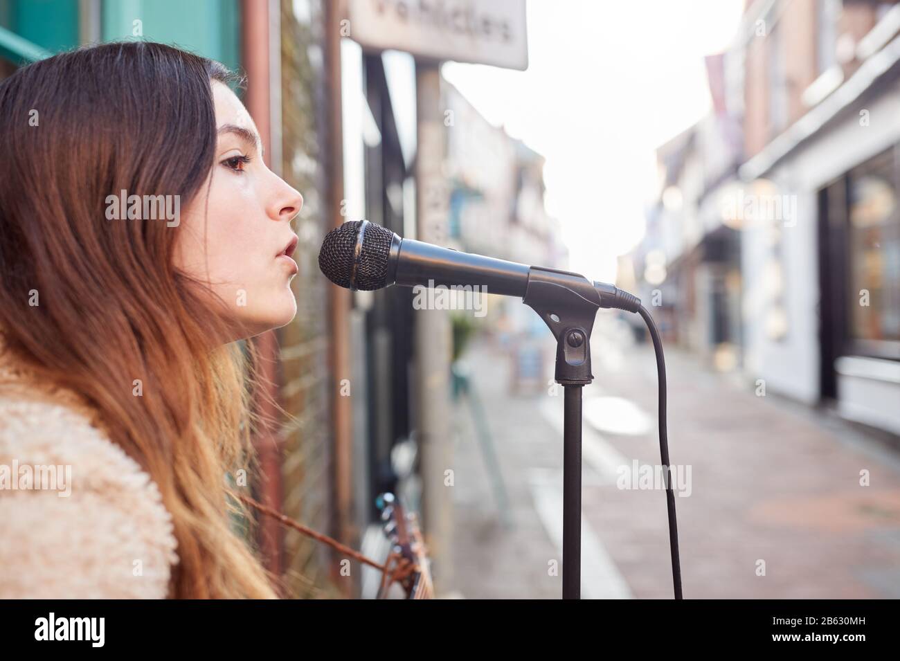 Female Musician Busking Playing Acoustic Guitar And Singing Outdoors In Street Stock Photo