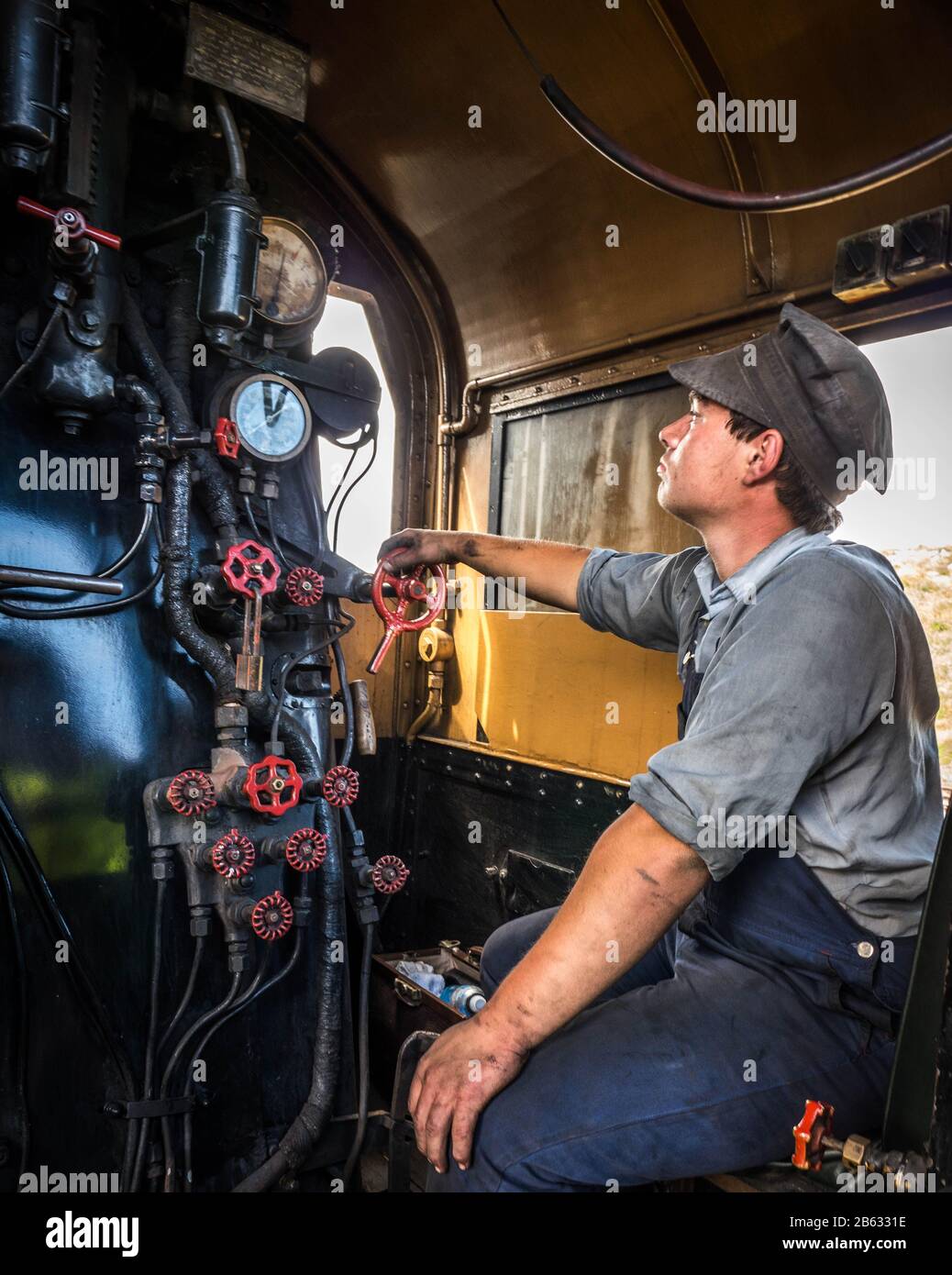 Young man volunteering as a steam engine fireman and engineer sitting in steam locomotive engine looking out window with hand on controls. Stock Photo