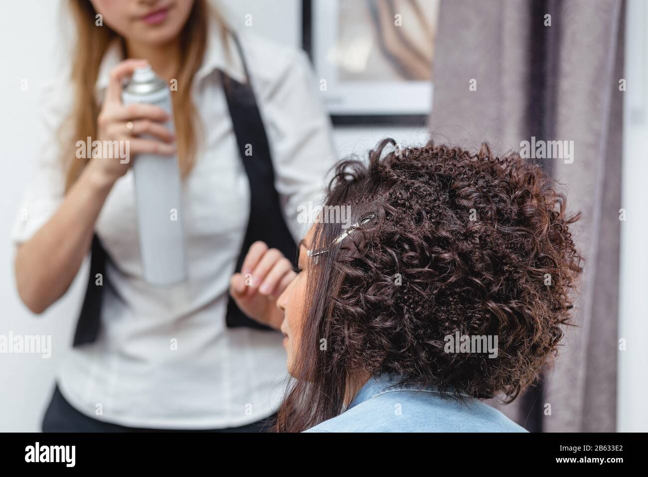 A professional hairdresser makes modern fine hairdo with the curls to the unusual appearance model of the middle East race Stock Photo