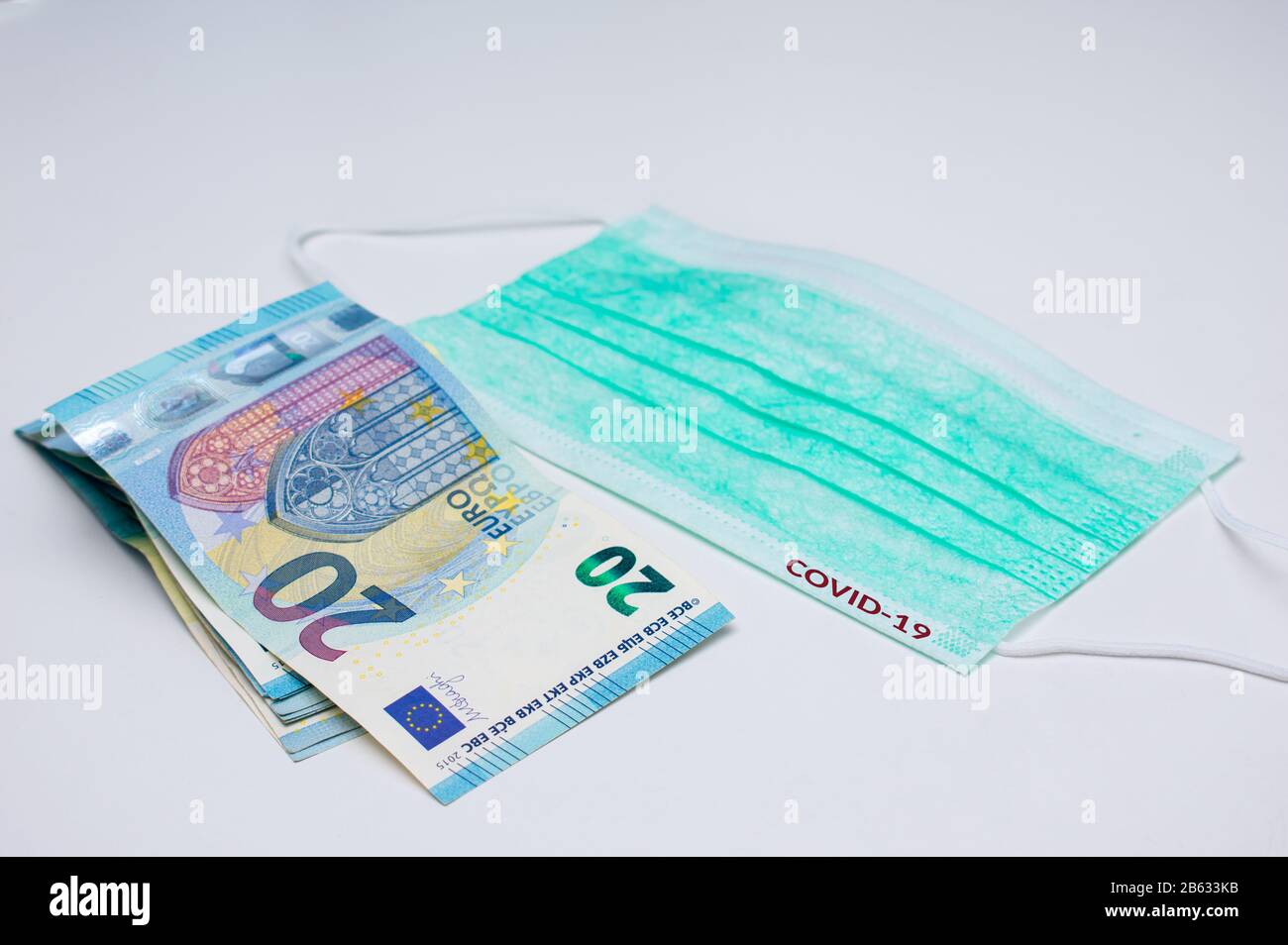 20 euro banknotes next to a medical face mask. The word COVID-19 is written in red on the mask Stock Photo