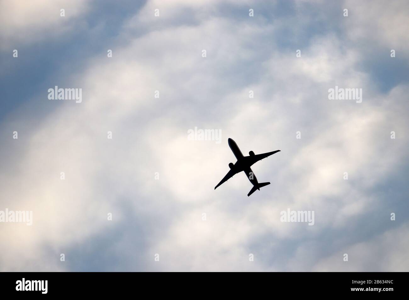 Airplane flying in the blue sky on background of white clouds. Silhouette of a commercial plane during the climb, travel and turbulence concept Stock Photo