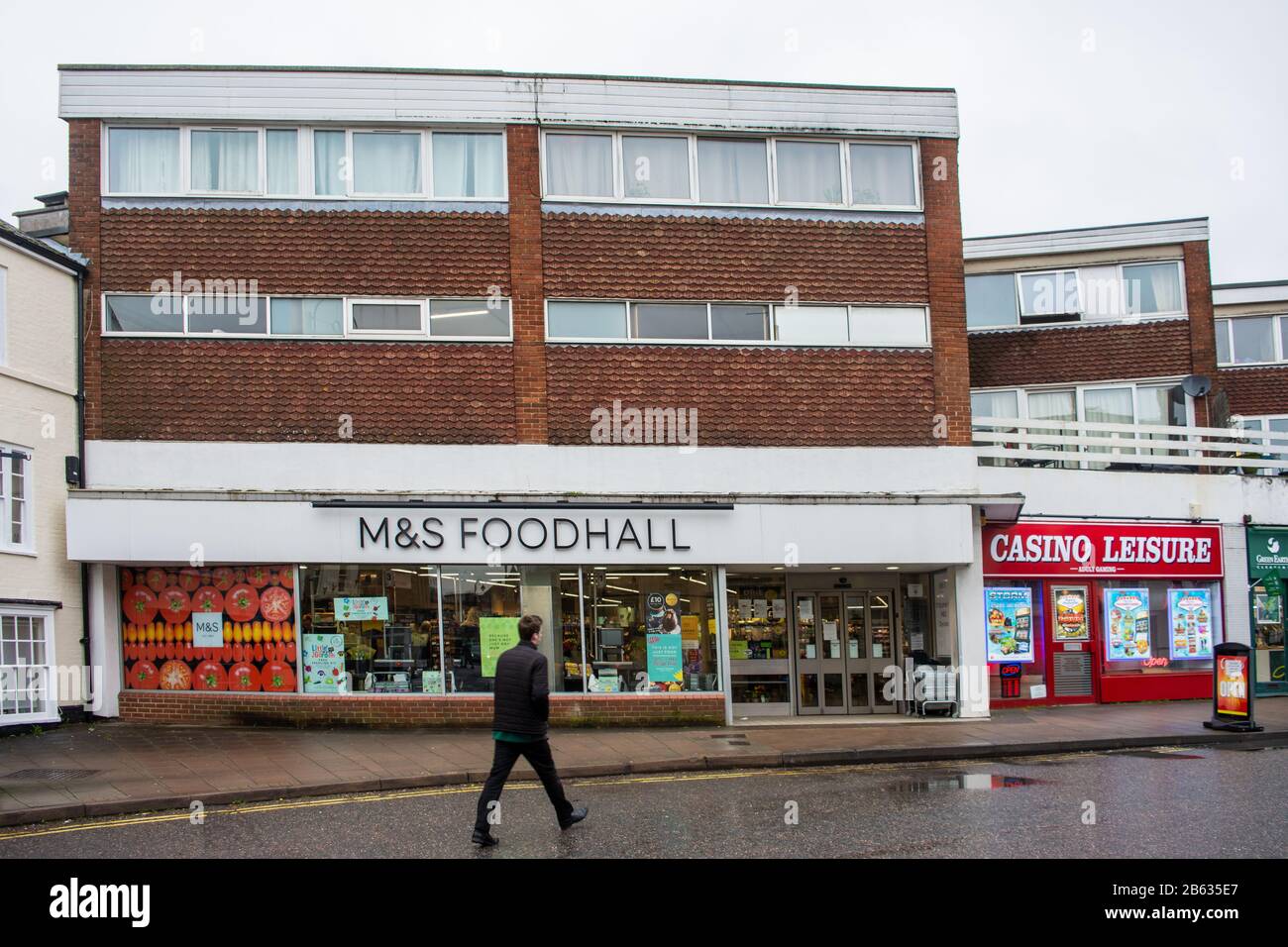 An M&S Foodhall shop underneath residential flats with a motion blurred pedestrian passing by Stock Photo