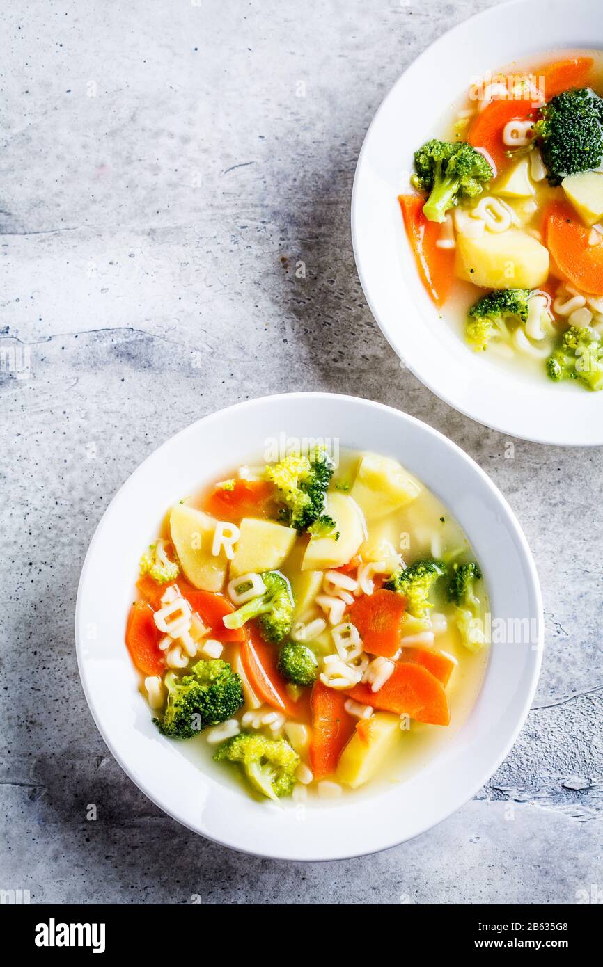 Healthy kids alphabet soup with vegetables and noodle letters in white plates. Baby food concept. Stock Photo