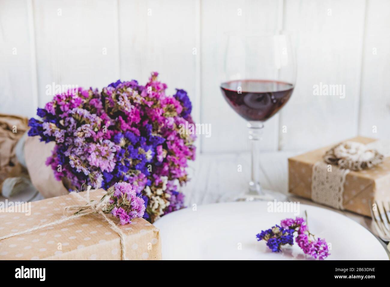 Table setting. Plate on wooden background with gift box, cutlery, a glass of red wine. Stock Photo