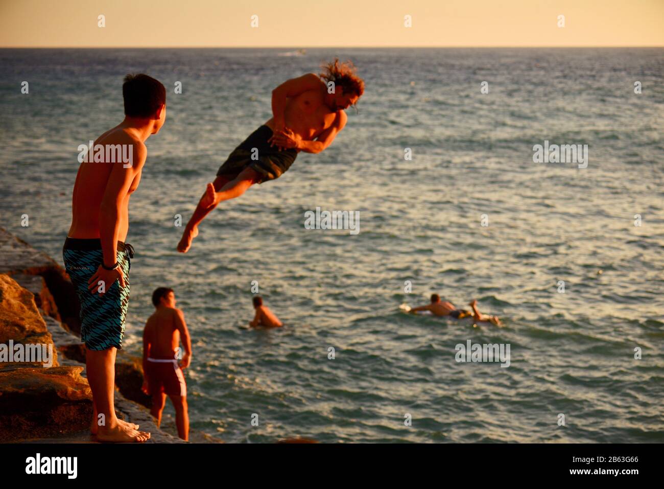 Cliff jumpers, wearing board shorts, jumping off ledge into ocean at China Walls on east side of Honolulu, Oahu Island, Hawaii, USA Stock Photo