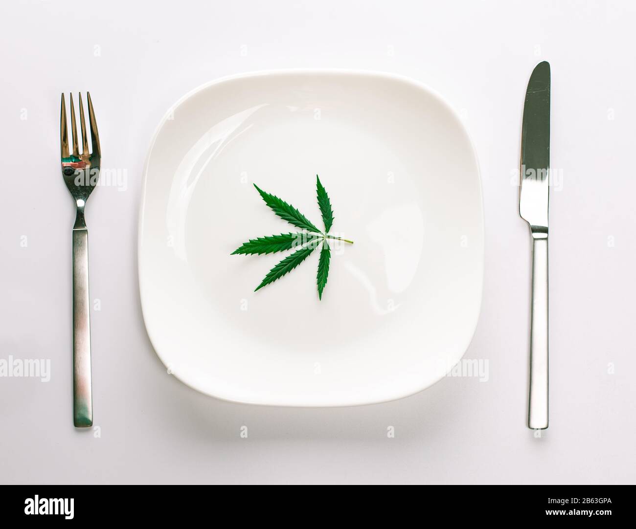Conceptual image of a green cannabis leaf on a white plate with a knife and fork isolated on a white background with copy space for text. Don't take d Stock Photo