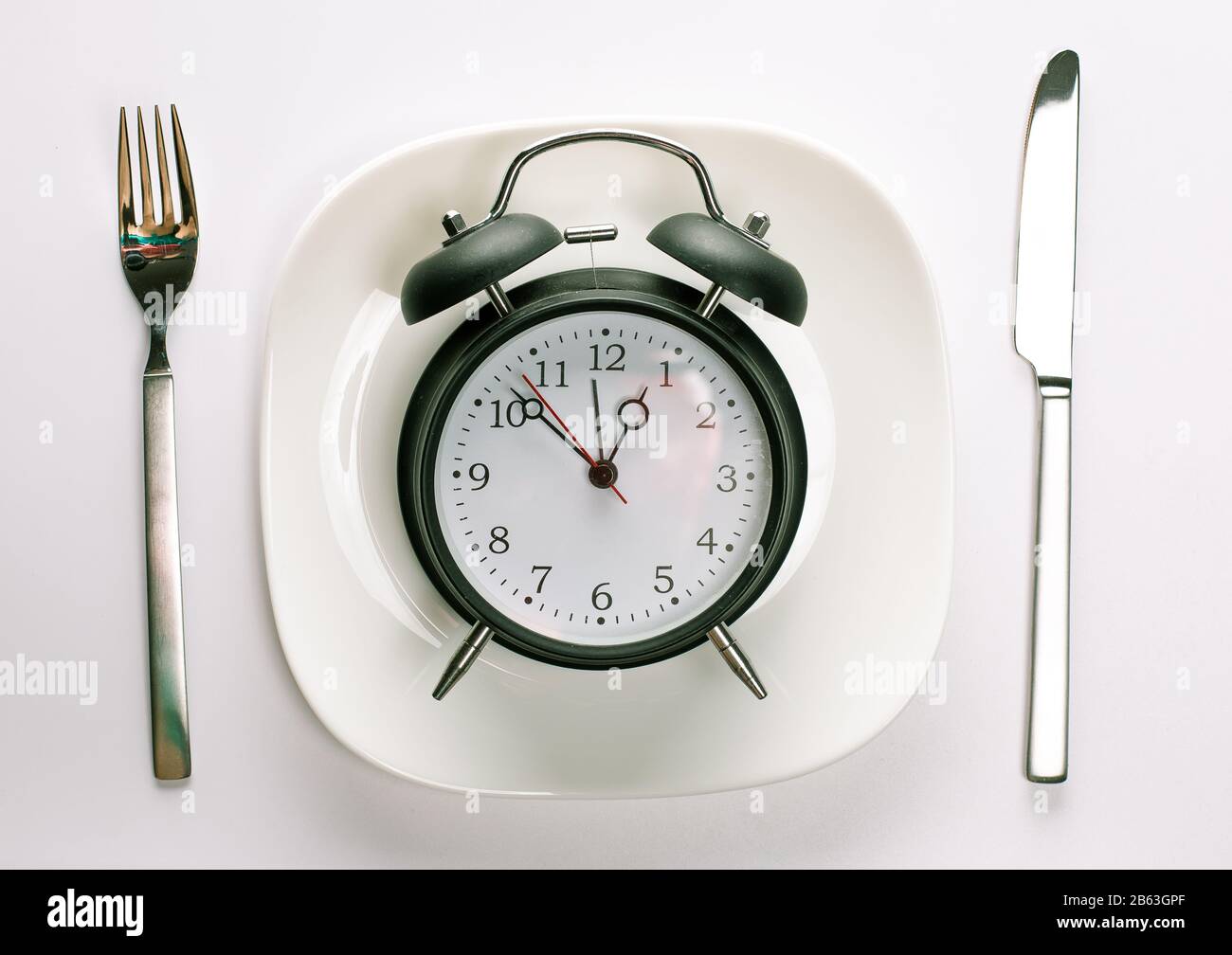 Time for lunch break concept. Alarm clock on a white plate with fork