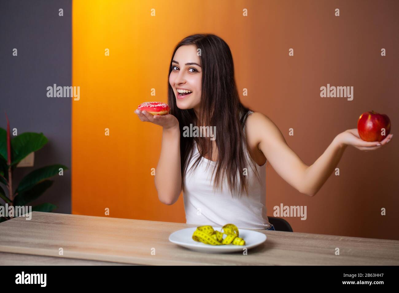 Portrait of a young beautiful girl who makes a choice between healthy food and harmful Stock Photo