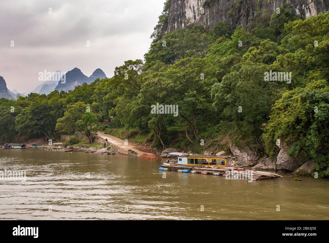Guilin, China - May 10, 2010: Along Li River. Long Barrel supported raft with construction tools anchored near point where road reaches water. Green f Stock Photo