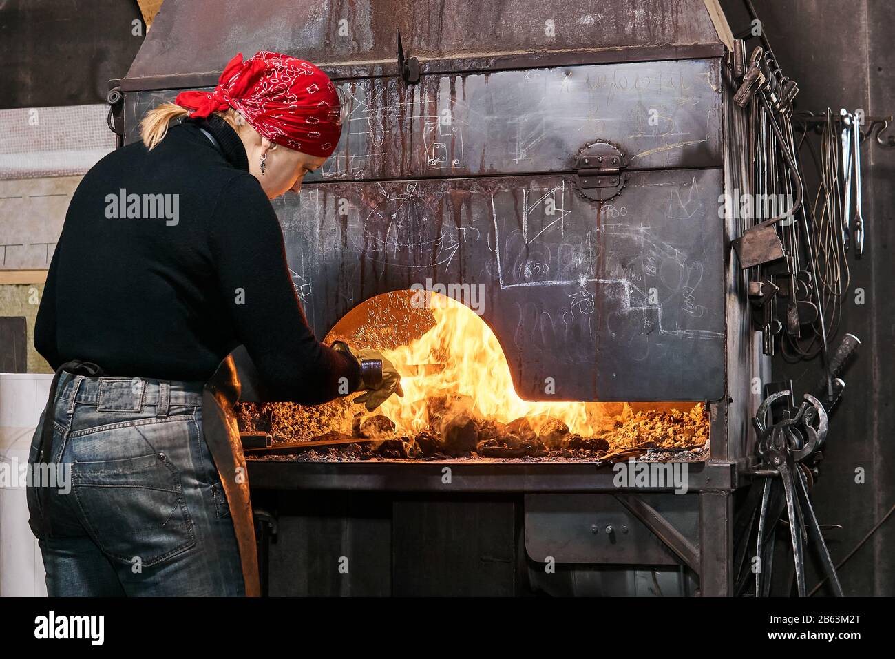 female metal artist is heating a workpiece in a blazing forge furnace Stock Photo