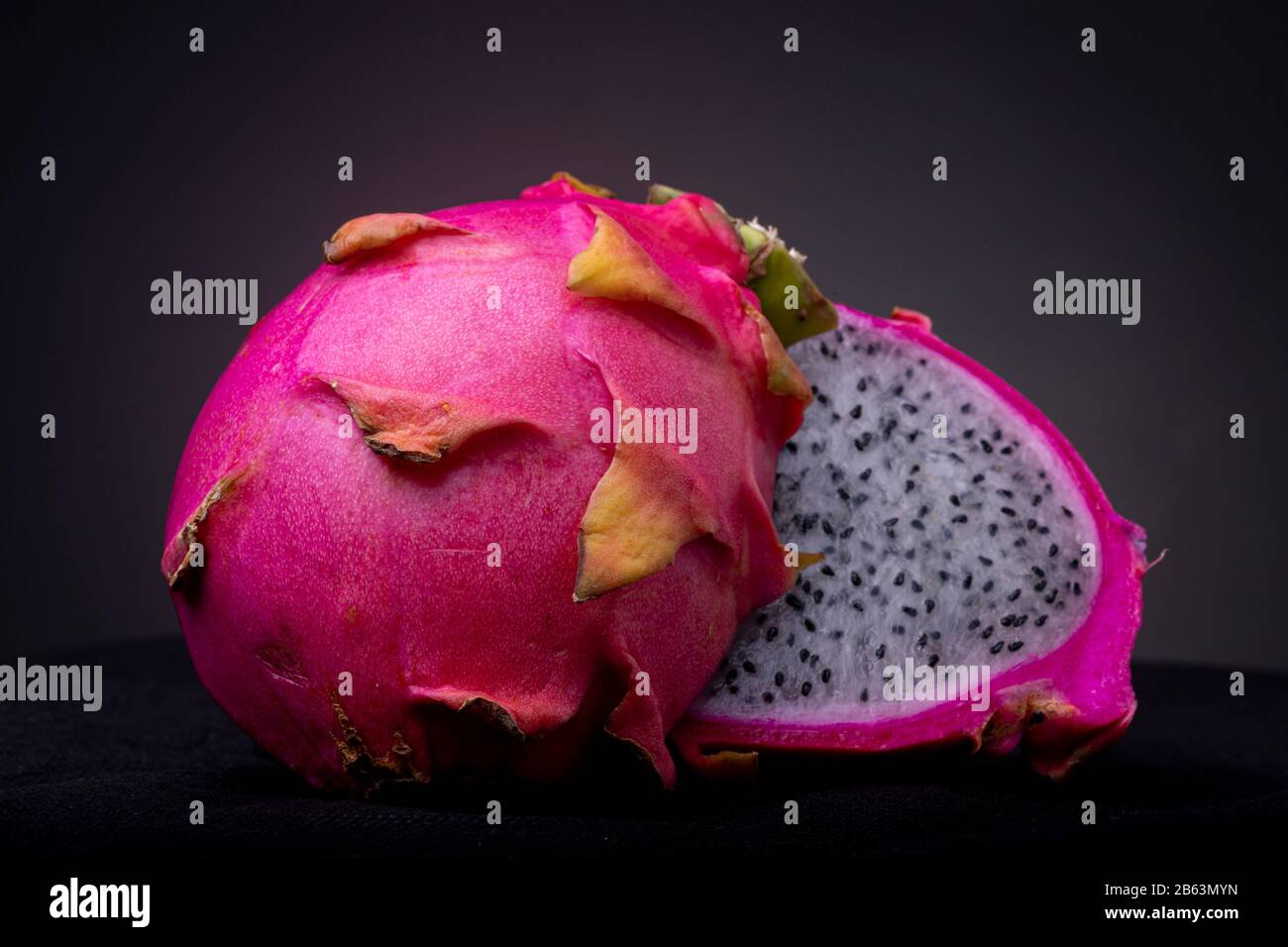Close up of two halves of a white-fleshed Pitaya or Dragon fruit with the outer shell and also white pulp with black seeds insides on a black surface Stock Photo