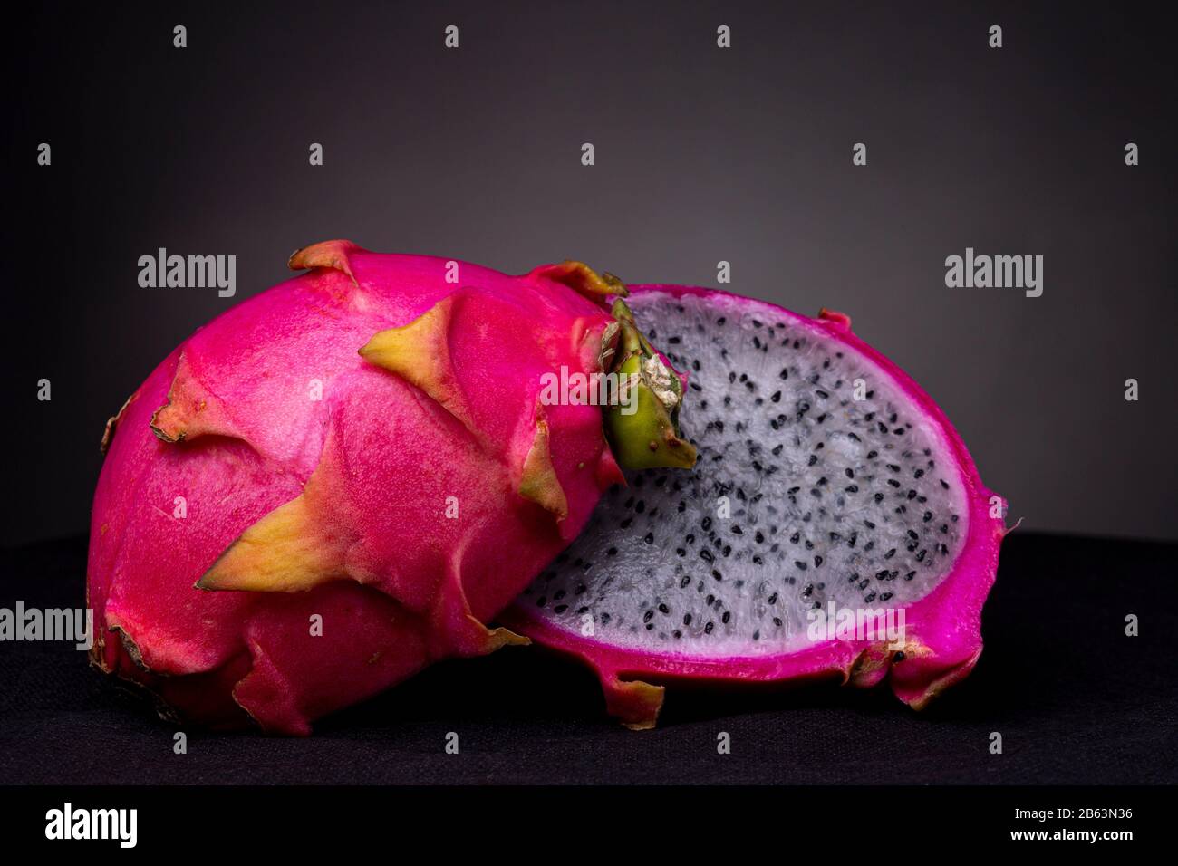 Two halves of white-fleshed Pitaya or Dragon fruit with the outer pink magenta scaly outer shell and white pulp with black seeds insides Stock Photo