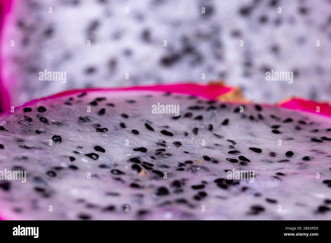 Close up macro view of white pulp and black seeds  of white-fleshed Pitaya or Dragon fruit with other half out of focus blurred in the background Stock Photo