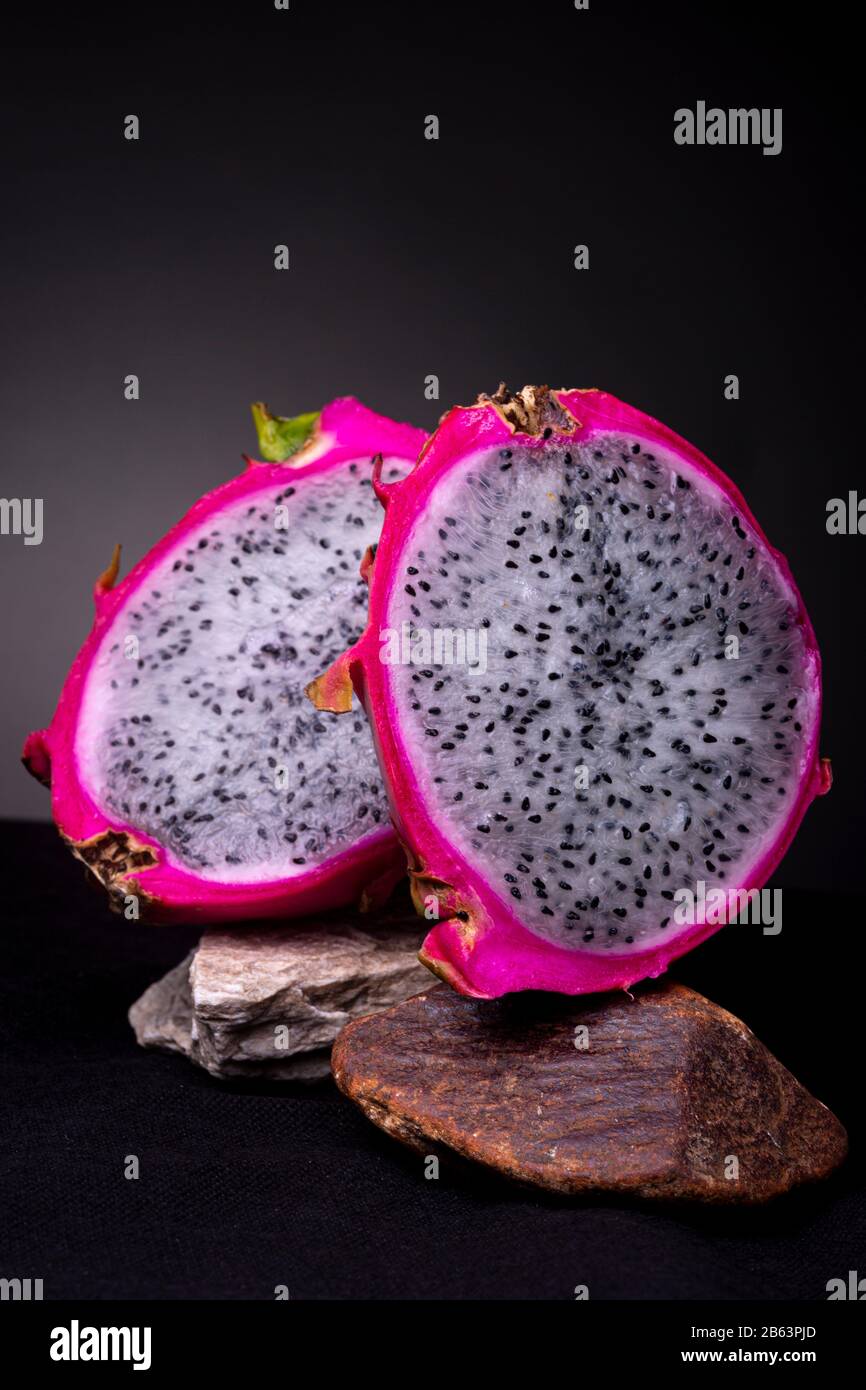 Opened up white-fleshed Pitaya or Dragon fruit displayed on two rocks with the outer skin and also white pulp with black seeds insides Stock Photo
