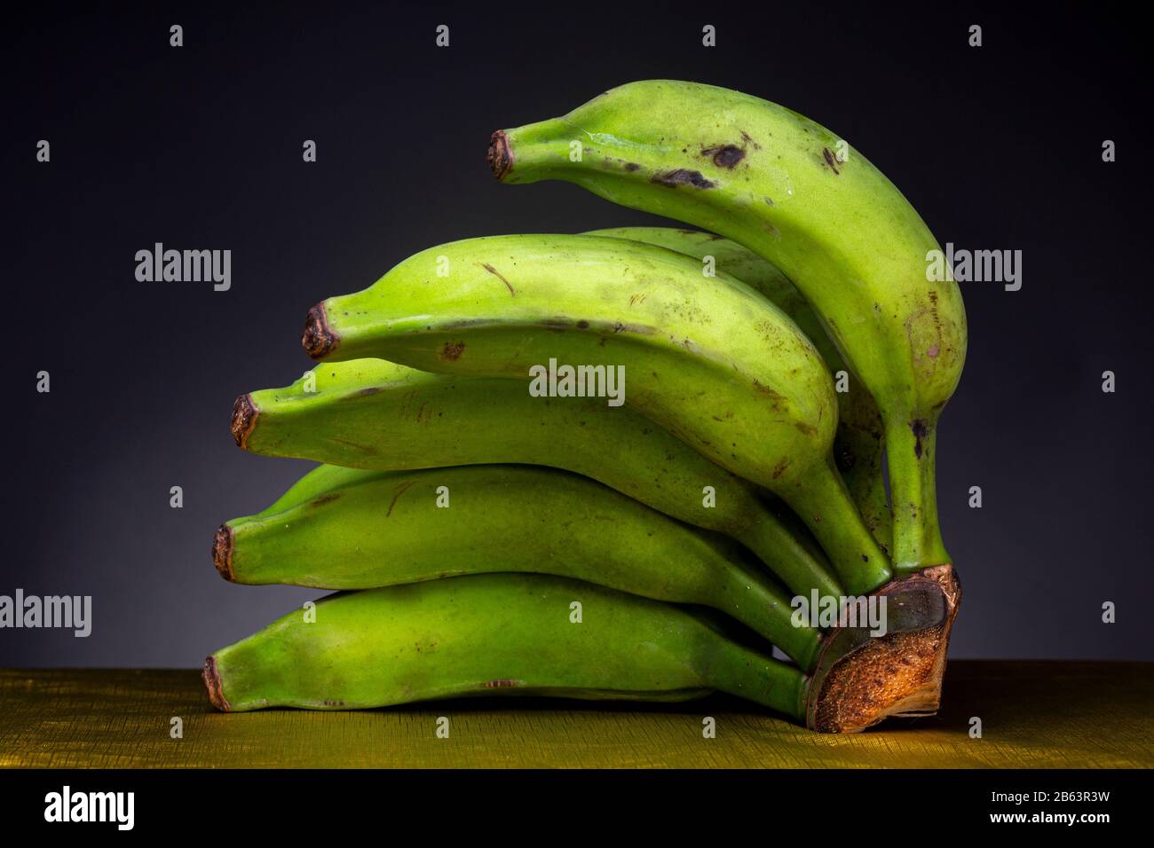 Brightly lit vibrant green banana on a gold coloured flimsy surface with  dark grey studio background Stock Photo - Alamy