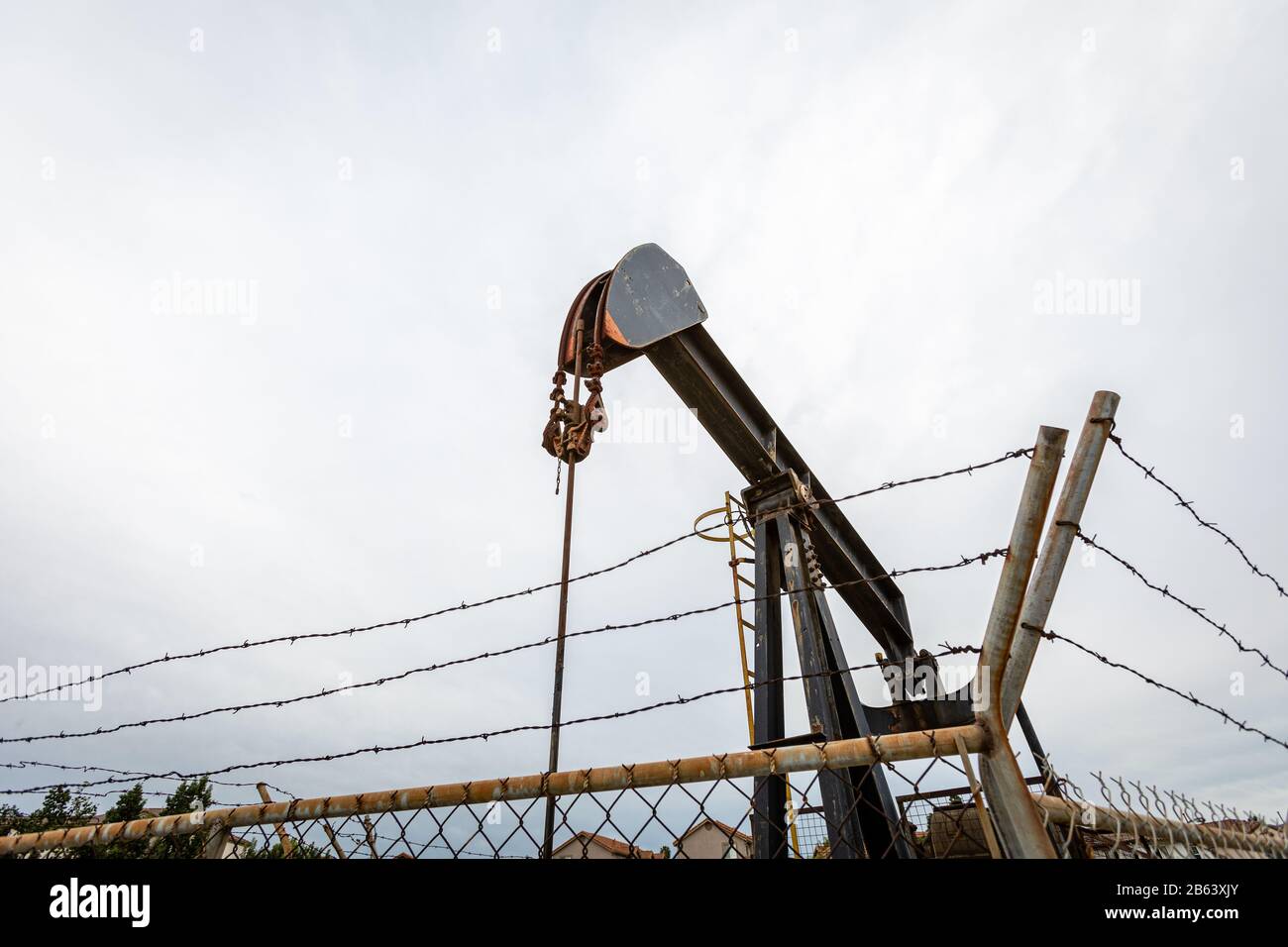Oil Pump in Cloudy Rough Weather with Chain Link Fence Stock Photo