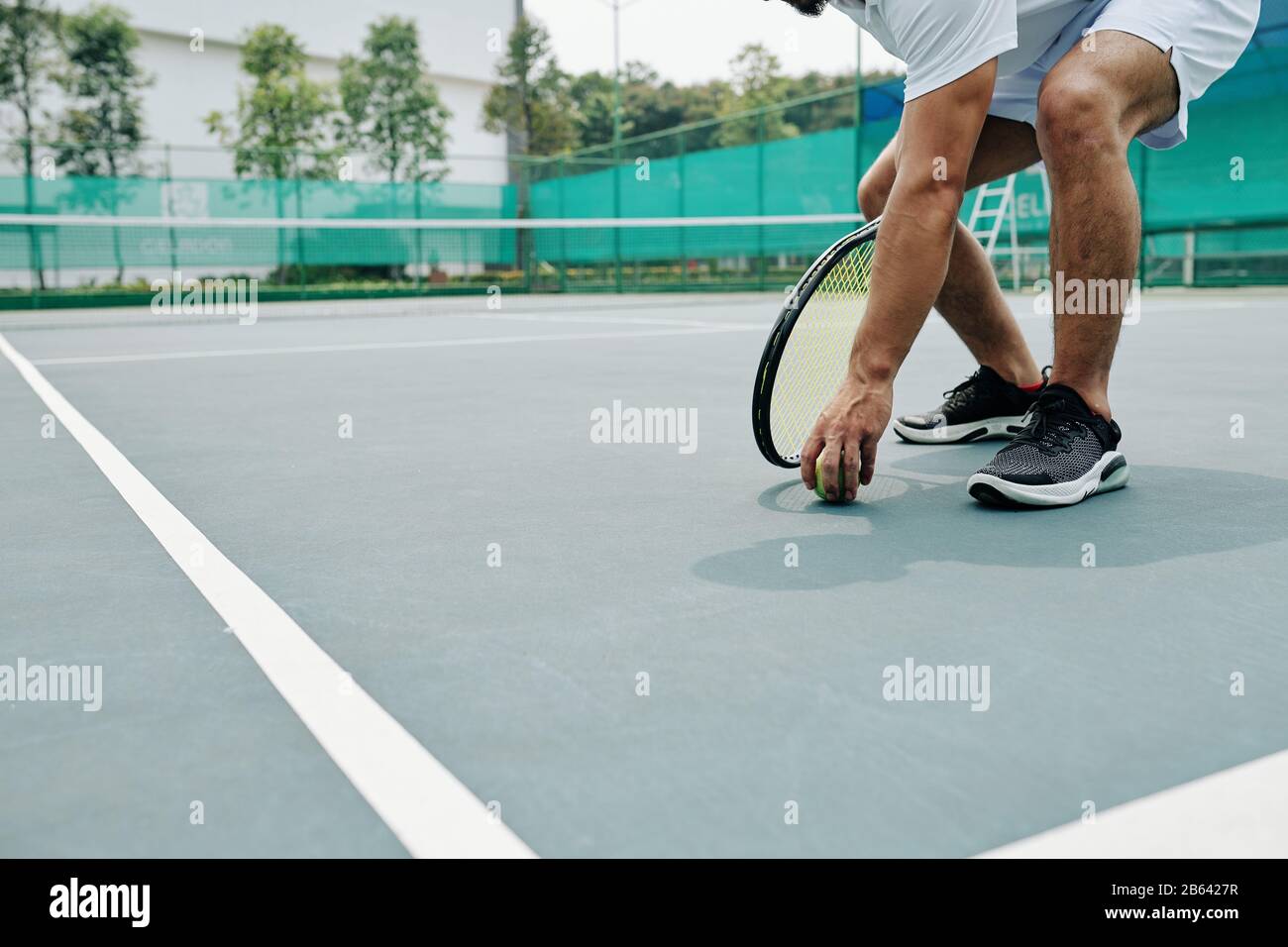 Tennis player bending to take ball from the ground Stock Photo