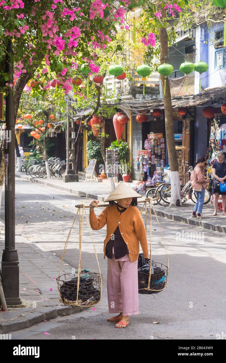 Vietnam Hoi An - Vietnamese woman - street vendor holding traditional shoulder baskets on the street of Hoi An. Southeast Asia. Stock Photo